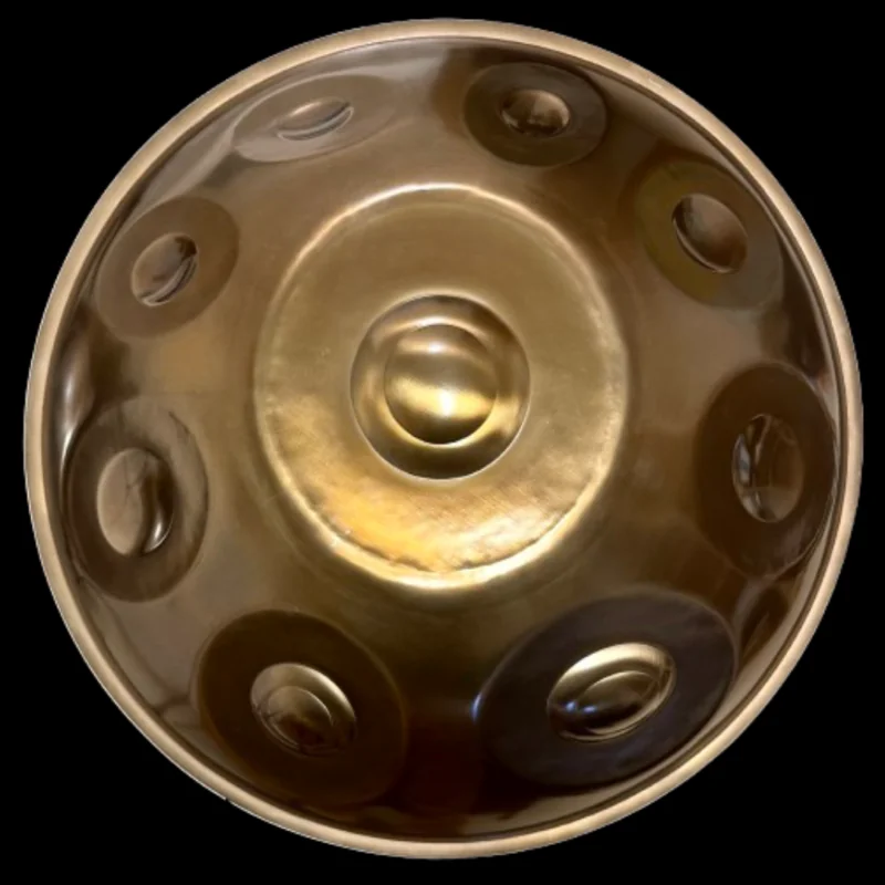 Handpan Yishama F2 Astronaut visto desde arriba sobre fondo negro: superficie dorada brillante, el ding en el centro y una docena de zonas de notas visibles.